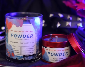 Könnte beinhalten: Zwei rote und blaue Kerzen mit dem Text "Ma Meilleure Ennemie Powder Inspired Candle" und "Black Rose + Red Candy Peach". Die größere Kerze befindet sich in einem Glasgefäß und die kleinere Kerze in einer Metalldose.