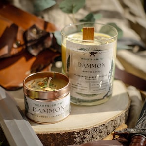 以下が含まれることがあります： 「HEARTS-SMITH」DAMMON INSPIRED CANDLEというラベルのついた2本のキャンドル。大きなキャンドルは、木製の芯が入った透明なガラス瓶に入っています。小さなキャンドルは、蓋付きの金属製の缶に入っています。両方のキャンドルは黄色のワックスで、「FLICKERING AMBER + CREAMY PISTACHIO」の香りが付いています。