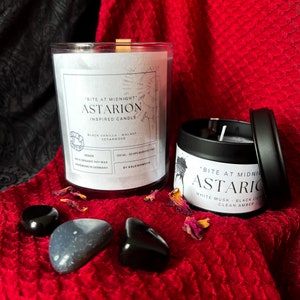 May include: Two candles with black labels and white text. The candle on the left is in a clear glass jar and says "Bite at Midnight Astarion Inspired Candle Black Vanilla Walnut Cedarwood Vegan 100% Organic Soy Wax Handmade in Germany 300 ml - 50 hrs Burning Time By Kaleidomeow". The candle on the right is in a black tin and says "Bite at Midnight Astaric White Musk Black Lily Clean Amber".