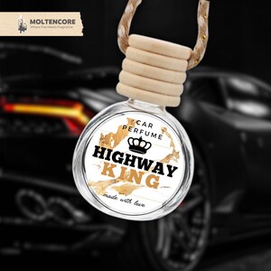Könnte beinhalten: Ein runder, gläserner Auto-Lufterfrischer mit einem weißen Etikett, auf dem "CAR PERFUME HIGHWAY KING made with love" steht. Das Etikett hat eine goldene Krone und ein goldenes Marmormuster.