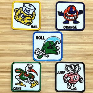 May include: Five colorful embroidered patches with team mascots and slogans. The patches feature a tiger, a wave, a bird, a badger, and a smiling orange character. The slogans are "Hail", "Roll", "Cane", "Jump", and "Orange".