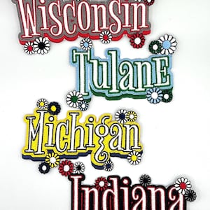May include: Embroidered patches featuring the names "Wisconsin," "Tulane," "Michigan," and "Indiana." Each patch has a unique color scheme and is adorned with daisy-like flower embellishments. The patches are designed with a retro aesthetic.