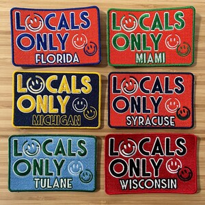 May include: Six embroidered patches with the text "Locals Only" in different colors and fonts. Each patch features a smiley face and the name of a city or university: Florida, Miami, Michigan, Syracuse, Tulane, and Wisconsin.
