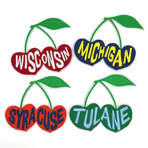 May include: Four embroidered patches in the shape of cherries. Each cherry pair features a different state or university name: Wisconsin, Michigan, Syracuse, and Tulane. The cherries are red, orange, green, and blue, with green leaves and stems.