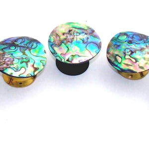 May include: Five circular cabinet knobs featuring iridescent abalone shell inlays with swirling patterns of green, blue, and pink. Each knob has a metallic base, with four showing a silver-tone finish and one showing a dark black finish.
