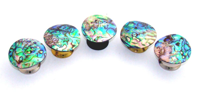 May include: Five circular cabinet knobs featuring iridescent abalone shell inlays with swirling patterns of green, blue, and pink. Each knob has a metallic base, with four showing a silver-tone finish and one showing a dark black finish.
