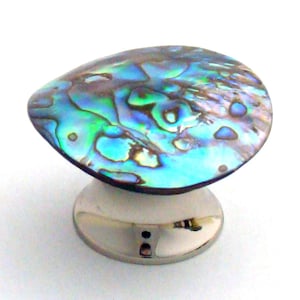 May include: A cabinet knob featuring a polished, iridescent abalone shell inlay with swirling patterns of blue, green, and purple hues. The shell is mounted on a smooth, circular, silver-toned metal base with a reflective finish and a central screw hole.