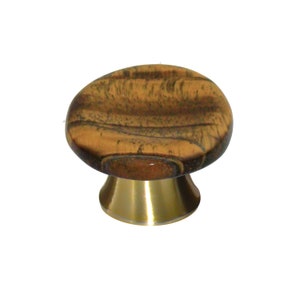 May include: A cabinet knob featuring a round, polished top with a brown and tan wood grain pattern. The base of the knob is made of a smooth, metallic gold-toned material with a flared, conical shape that connects to the circular top piece.