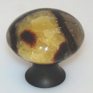 May include: A decorative cabinet knob with a brown, yellow, and cream-colored stone top. The stone has a unique pattern with dark brown streaks and a dark brown center. The knob is mounted on a dark brown metal base.