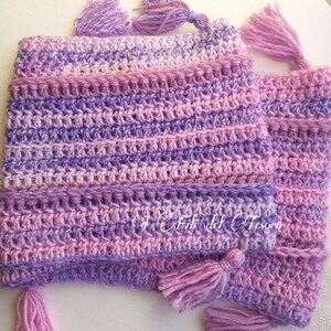 May include: A purple and pink crocheted hat with tassels. The hat is made with a variegated yarn and has a striped pattern.