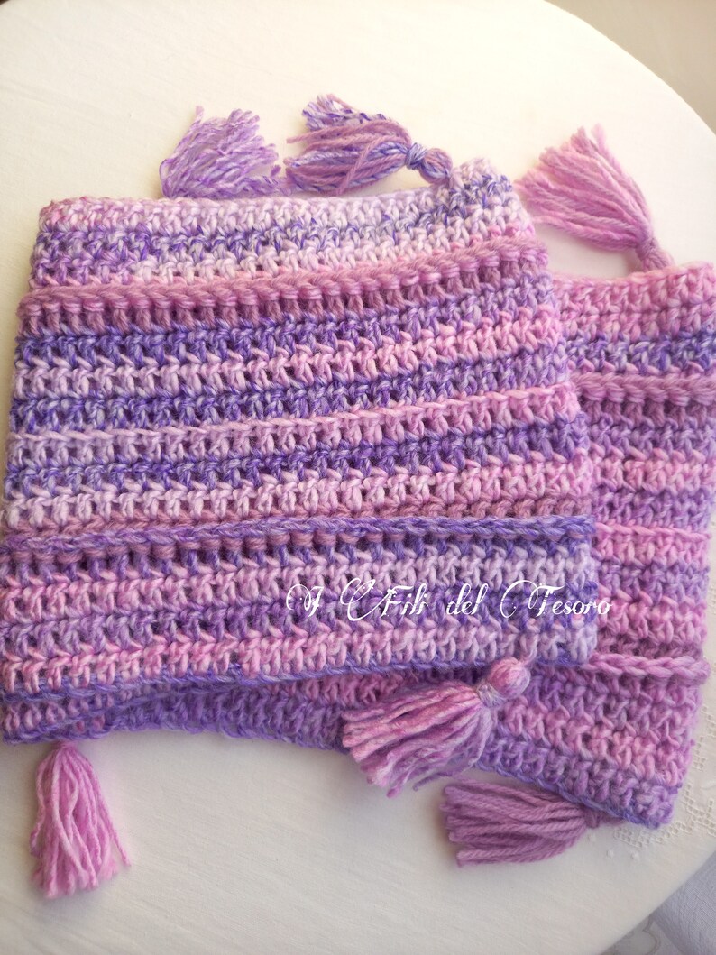 May include: A purple and pink crocheted hat with tassels. The hat is made with a variegated yarn and has a striped pattern.