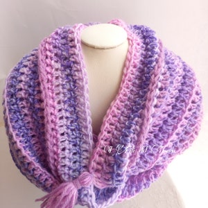 May include: A crocheted cowl scarf in shades of purple and pink with a long tassel. The scarf is made with a soft, textured yarn and has a simple, elegant design.