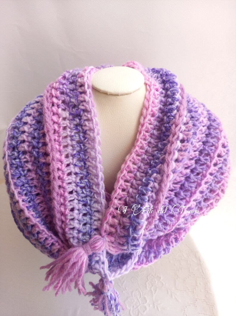 May include: A crocheted cowl scarf in shades of purple and pink with a long tassel. The scarf is made with a soft, textured yarn and has a simple, elegant design.