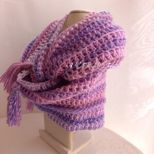 May include: A purple and pink crocheted shawl with a fringe tassel. The shawl is displayed on a white mannequin.