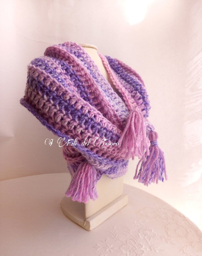 May include: A purple and pink crocheted scarf with long tassels. The scarf is displayed on a white mannequin.