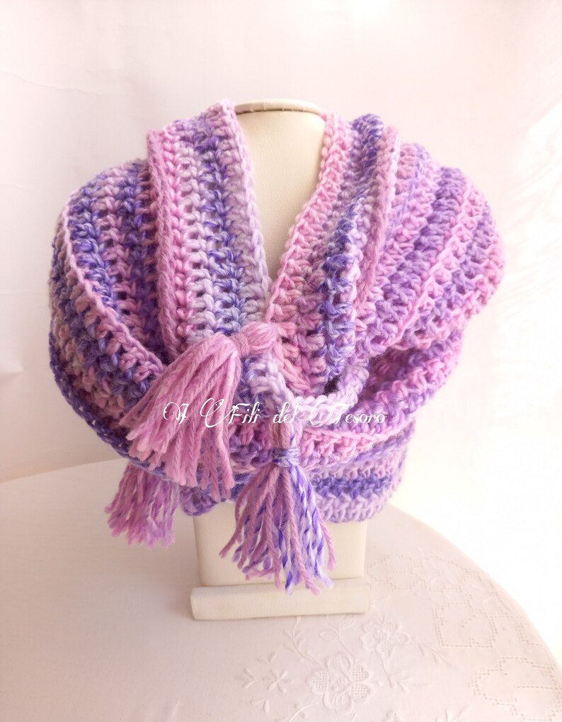 May include: A crocheted scarf in shades of pink and purple with long tassels. The scarf is displayed on a white mannequin.