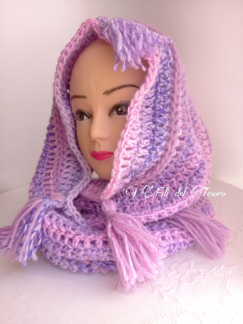 May include: A purple and pink crocheted hooded scarf with tassels. The scarf is made with a soft, textured yarn and has a loose, flowing design.