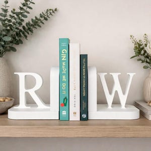 a pair of white initial bookends, R W, styled on a wood shelf with books in between.