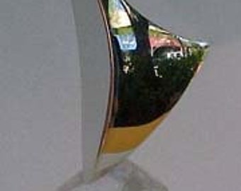 May include: A silver abstract sculpture with a sharp, angular design. The sculpture is mounted on a clear, faceted crystal base.