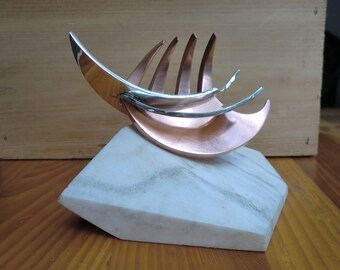 May include: A silver and copper sculpture of a stylized leaf, mounted on a white marble base.