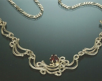 May include: A gold necklace with a delicate, intricate design featuring a single red gemstone. The necklace has a chain link style and a pendant with a curved, flowing shape.