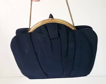 May include: A black fabric evening bag with a gold metal frame and a black top closure. The bag has a chain strap.