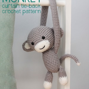 May include: A gray crocheted monkey toy with white accents hanging from a white wooden ladder. The monkey is holding onto the ladder with its arms and has a long tail. The text "CHEEKY MONKEY curtain tie-back crochet pattern" is visible at the top of the image.