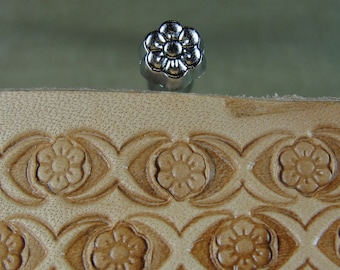 May include: A close-up of a silver flower-shaped leather stamping tool. The tool is used to create decorative patterns on leather.