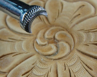 Op de afbeelding: Een lederbewerkingstool met een sikkelvormig mes. De tool wordt gebruikt om een decoratief patroon op een stuk leer te maken.