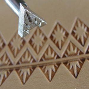 Pode incluir: Uma ferramenta de carimbo de couro de metal com um design de estrela. A ferramenta é usada para criar um padrão em um pedaço de couro.