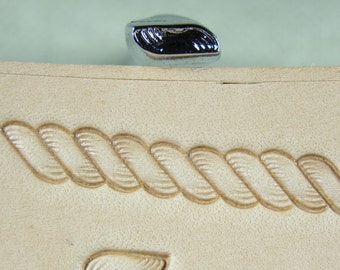 Op de afbeelding: Een close-up van een lederen stempelgereedschap met een touwontwerp. Het gereedschap is gemaakt van metaal en heeft een gepolijste afwerking. Het touwontwerp is in een stuk leer gegraveerd.