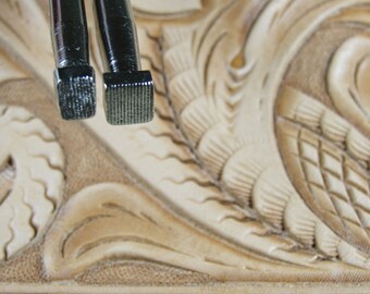 May include: Two metal leather carving tools with a textured surface. The tools are used to create designs in leather.