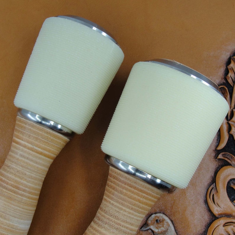 May include: Two leather working mallets with wooden handles and white rubber heads. The mallets have a silver metal band around the top of the head.