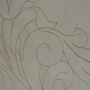 May include: Close-up of a beige surface with a detailed, swirling floral pattern in a warm brown color. The design features stylized leaves and scroll-like elements, creating a textured, decorative effect.