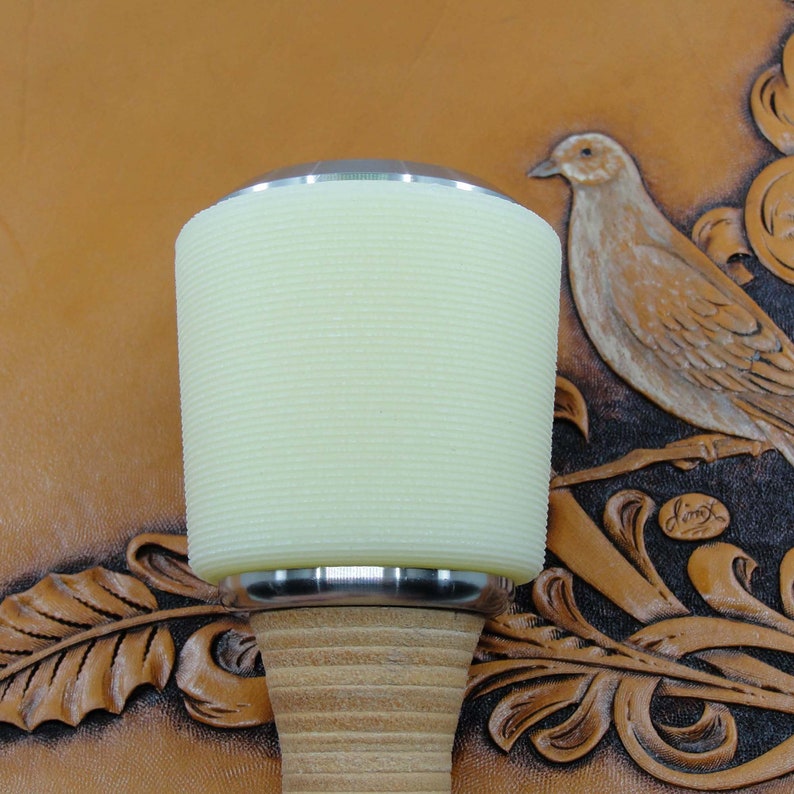 May include: A white leather working mallet with a wooden handle. The mallet has a ribbed surface and a silver metal band around the top.
