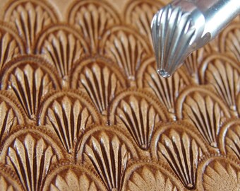 Op de afbeelding: Close-up van een leerbewerkingstool die een herhalend waaiervormig patroon creëert op een stuk bruin leer. De tool is zilverkleurig en heeft een getextureerd, afgerond uiteinde. Het leer heeft een gedetailleerd, reliëf ontwerp.