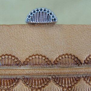 May include: A close-up of a leather stamping tool with a decorative design. The tool is made of metal and has a silver finish. The design is a series of small circles arranged in a fan shape.