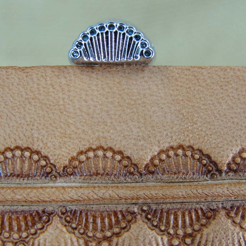 May include: A close-up of a leather stamping tool with a decorative design. The tool is made of metal and has a silver finish. The design is a series of small circles arranged in a fan shape.