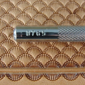 May include: Close-up of a silver leather stamping tool with the number "D765" engraved on the side.