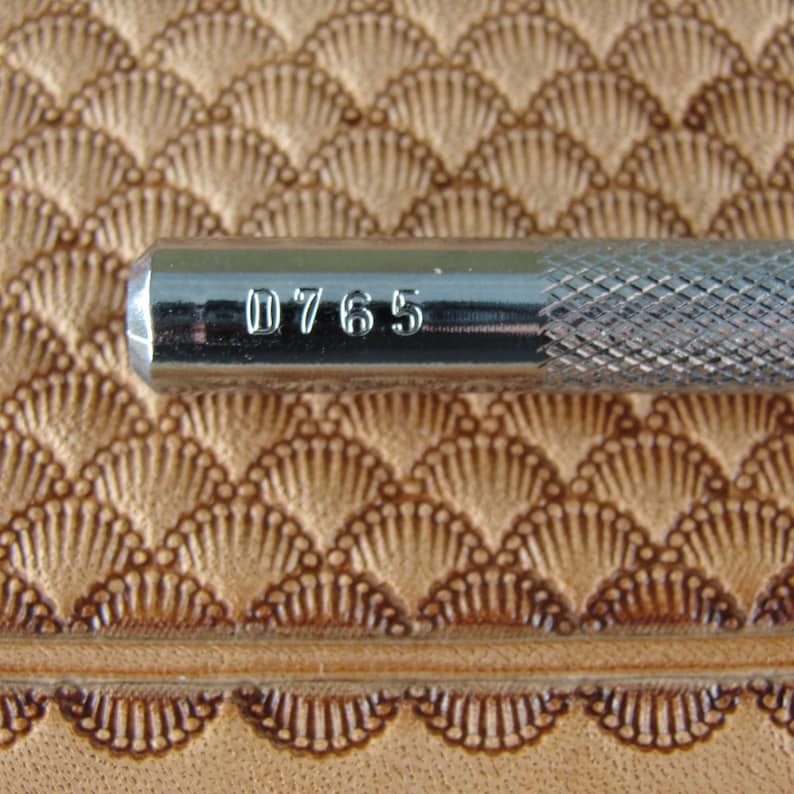 May include: Close-up of a silver leather stamping tool with the number "D765" engraved on the side.