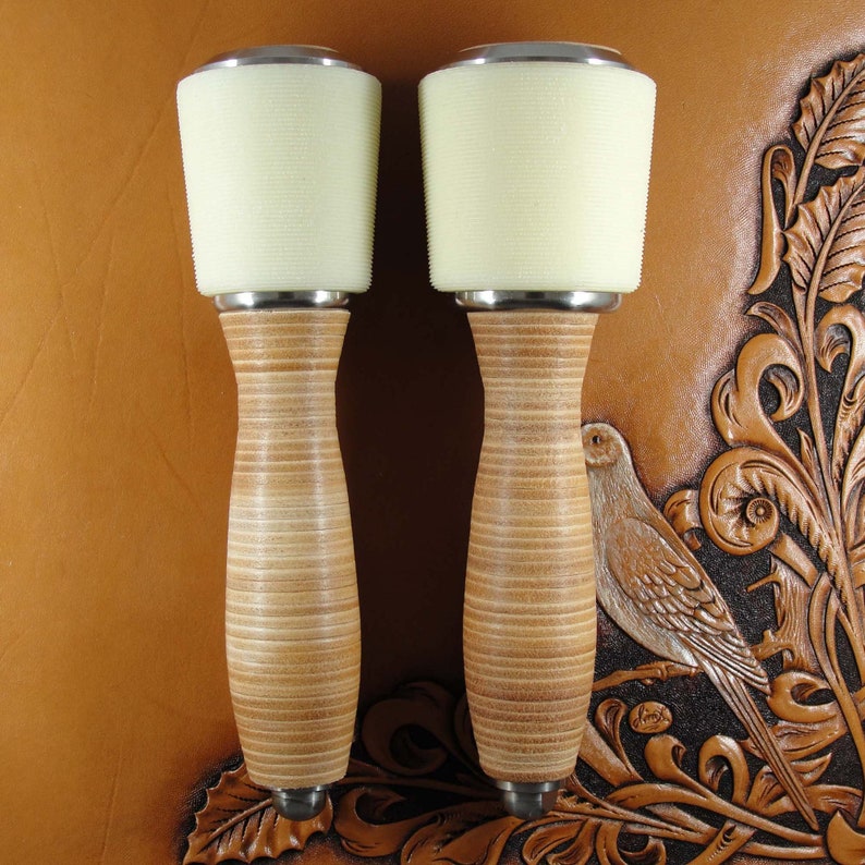 May include: Two leather working mallets with white rubber heads and wooden handles. The mallets are on a brown leather background.