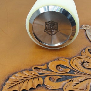 May include: A close-up of a leather working tool with a white foam handle and a stainless steel head. The head has a logo with the text "ZHONGJIANG" in a shield shape.