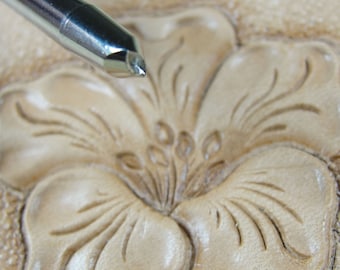 May include: Close-up of a leather carving tool poised over a floral design. The tool is silver and the leather is a light tan color. The carved flower has detailed petals and a textured surface, showcasing the craft of leatherwork.
