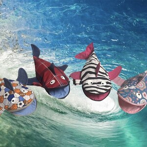 May include: Four plush shark toys with different fabric patterns. The sharks are red, black and white, blue and white, and orange and blue. The sharks have open mouths and big eyes.