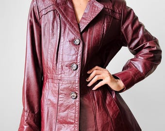 Può includere: Giacca in pelle bordeaux con colletto a revers e chiusura a tre bottoni. La giacca ha maniche lunghe e vita aderente. La giacca è di colore rosso scuro e sembra vintage.