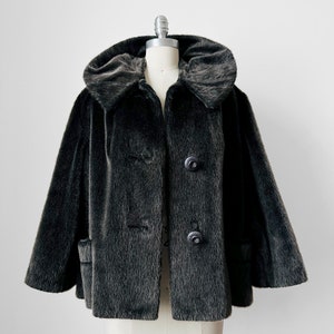 May include: A black faux fur jacket with a large collar and three buttons. The jacket has a slightly flared shape.