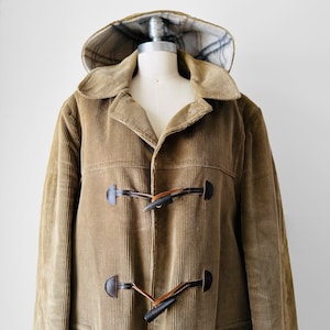 Peut inclure: Un manteau à capuche en velours côtelé marron avec une doublure à carreaux et des fermetures à boutons en bois.
