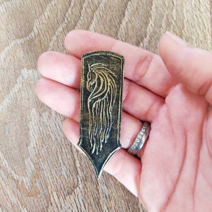 Puede incluir: Un marcapáginas de cuero negro y dorado con un diseño detallado de una cabeza de caballo.