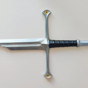 May include: A silver sword with a black handle and gold accents. The sword has a cross-shaped guard and a pointed blade.