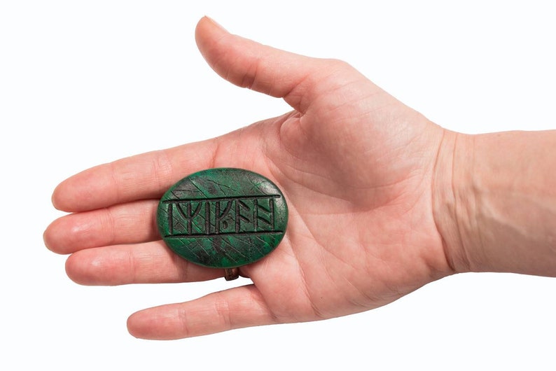 Op de afbeelding: Een groene, ovale steen met het woord "LYKEN" in het zwart gegraveerd.